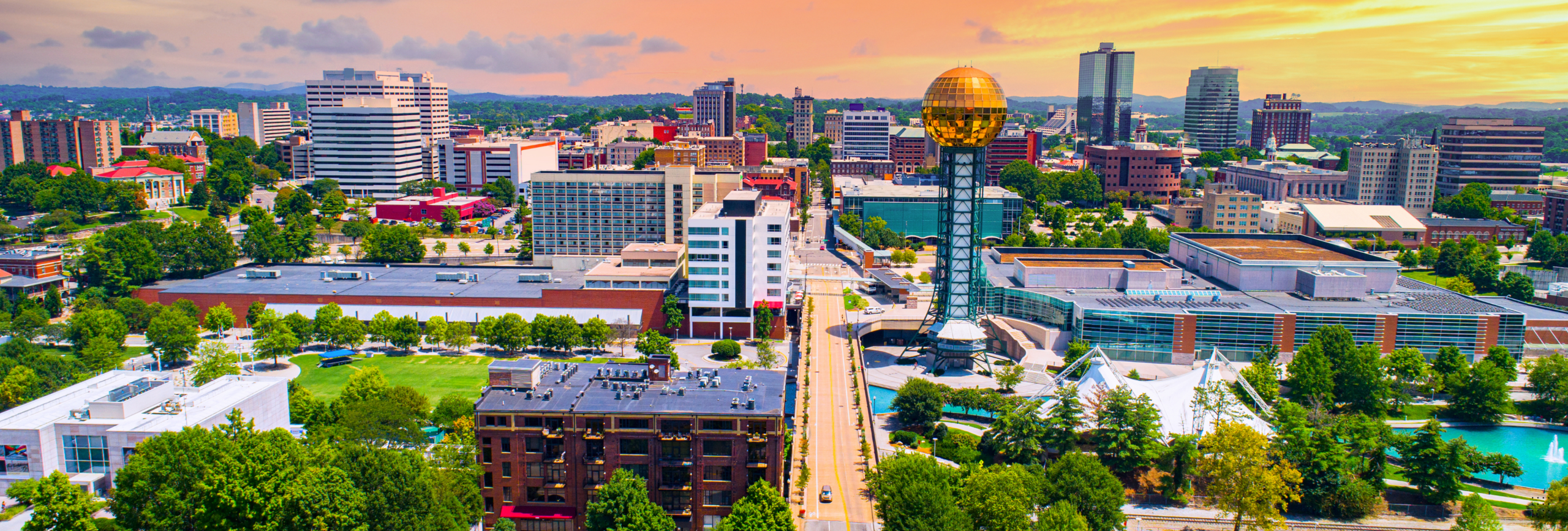 Aerial view of a vibrant cityscape at sunset, where modern buildings and the golden orb structure stand tall in contrast with lush green spaces. Amidst this urban beauty lies Franklin, noted for its serene retreats and mental health rehabs, under a picturesque cloudy sky.