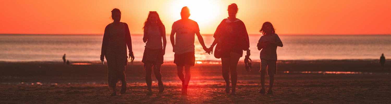 A silhouetted group of five strolls hand in hand along the beach at sunset, evoking a serene, family-friendly atmosphere. As the vibrant orange sky mirrors tranquility on the sea, its reminiscent of finding peace within oneself—like moments from Atlantas mental health treatment programs.