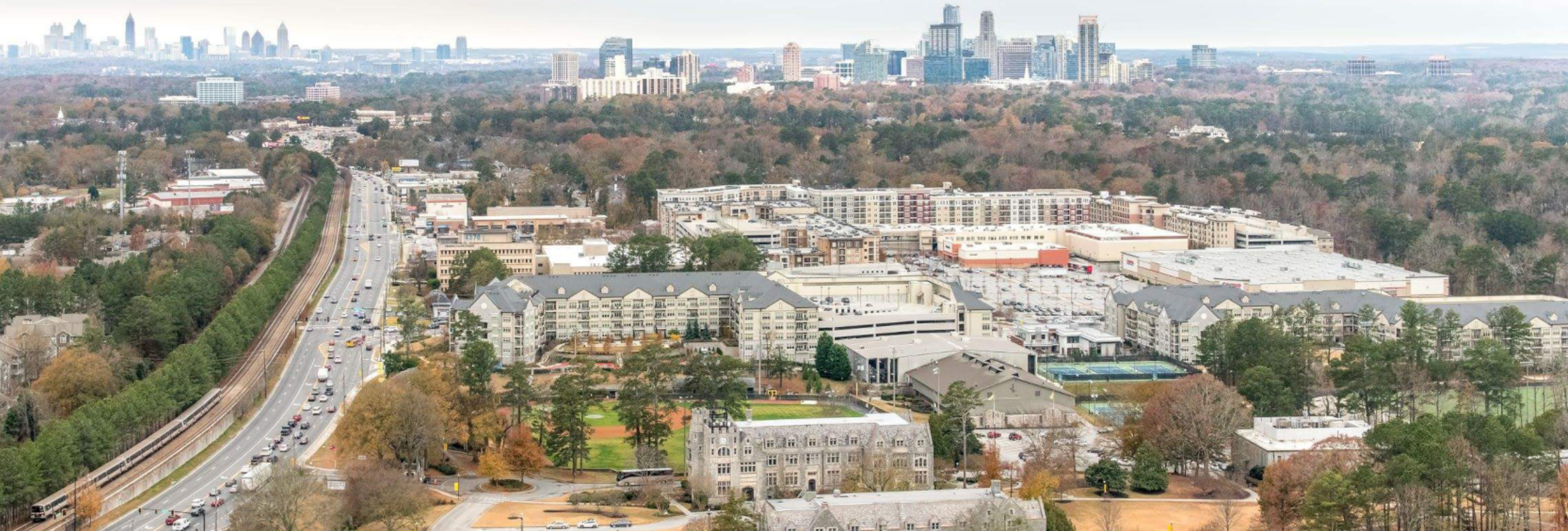 Aerial view of Mariettas cityscape with a mix of urban and suburban areas. Buildings and trees grace the foreground, with a road snaking alongside. In the background, the skyline stretches across the horizon under a cloudy sky, creating a serene setting that complements mental health treatment retreats nearby.