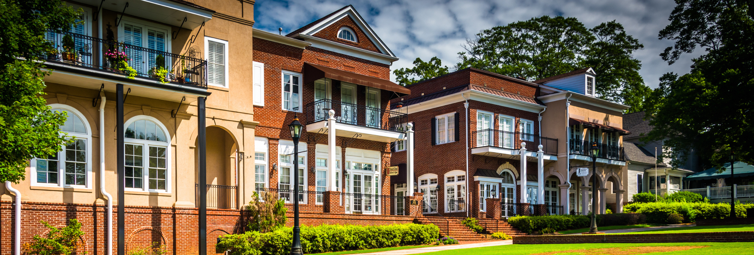 A row of elegant, multi-story buildings with balconies and large windows—ideal for serene living or spaces dedicated to Mental Health Treatment in Duluth—blends brick and stucco facades with greenery, all beneath a partly cloudy sky.